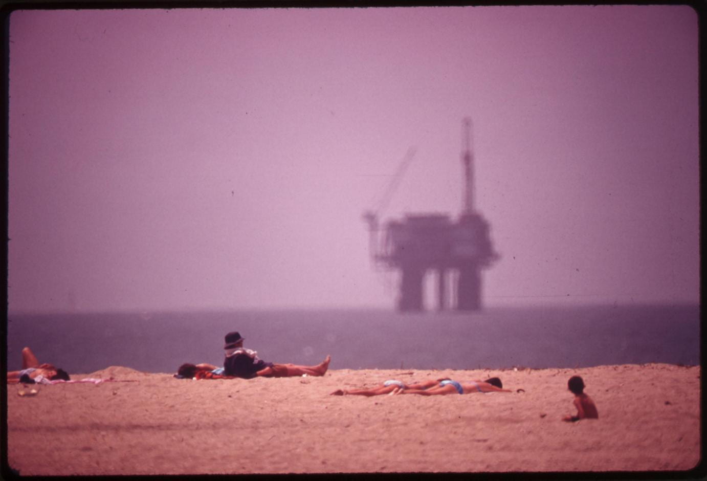 “Sunbathers at Huntington Beach and an oil platform offshore,” 1975.